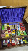 Photo showing multiple vintage metal toy cars organized in a wooden case with purple satin lining.