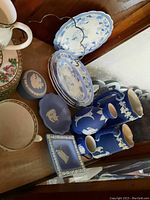 Overview of Wedgwood blue jasperware items and Adams Tunstall Bridewoods plates displayed on wooden surface showing pitchers, plates, lidded box, and cup