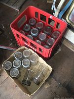 Full view of red Pop Shoppe crate filled with glass canning jars with metal lids and rings, next to a cardboard box with more jars.