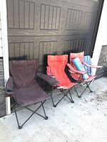 Four folding chairs (brown, orange, striped blue camp chairs; blue mesh lawn chair) arranged outside against garage door