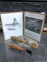 Photo showing hinged History of Fish Decoys frame open with black and white imagery and text behind the wood fish decoy and string holder on a reflective surface.