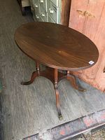 Full view of oval walnut side table showing oval top and three legs with brass feet.