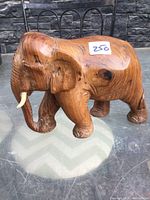 Side angled view of the hand carved solid wood elephant on a reflective surface showing tusks, ear, trunk, and body texture