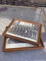 Two framed black and white group photos stacked on a glass table, showing labeled military groups in front of stone buildings, marked with lot number.