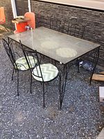 Photo showing the full patio dining set with rectangular wrought iron table topped with plexiglass and four wrought iron chairs, three with cushions.