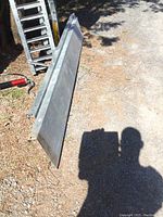 Steel ramp or shelf, showing full length laid on the ground with dirt and gravel surface.