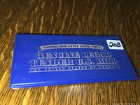 Blue commemorative folder closed with gold text stating 'Genuine Legal Tender U.S. Bill'.