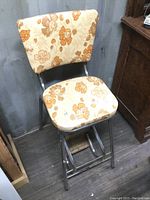 Front view of the vintage stool showing the chrome frame, floral upholstery, and fold-out wooden step.