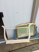 Two antique washstand backs; one cream with towel bar, one blue with mirror, placed outdoors on wooden surface
