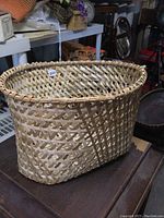 Side and front view of vintage woven wicker basket with oval shape and rounded rim, sitting on a wooden table in a storage setting.