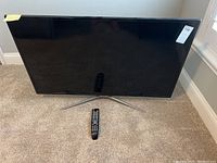 Front view of 45" Samsung TV on stand with remote on carpet
