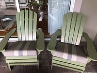 Front view of two green painted wooden Adirondack chairs with cushions.