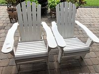 Front view showing two white painted Adirondack chairs on stone patio, wide armrests, slatted back and seat