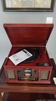 Top view showing the wooden Crosley stereo with record player, instruction manual on turntable, and remote control on the surface.
