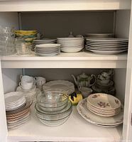 Full view of two shelves containing mixed dinnerware and glass pieces