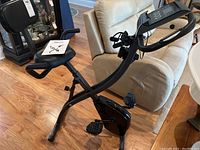 Full view of the Slim Cycle exercise bike showing black frame, seat with backrest, pedal straps, and digital console with handlebars.