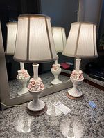 Pair of vintage petite lamps with white bases, pink and white floral porcelain clusters, and cream fabric shades against a mirror background.