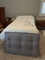 Front view of assembled adjustable bed base showing grey tufted footboard and mattress cover