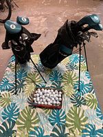 Two sets of ladies Ram Golf EZ3 golf clubs with stand bags displayed on a patterned mat along with a box of golf balls.