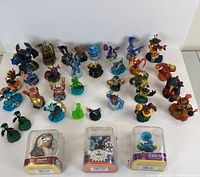 Photo showing majority of 35 Skylanders figures arranged in rows with three figures still in original plastic packaging, displayed on plain white background.