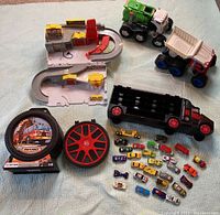 Overview of the lot showing diecast cars, toy trucks, playsets, and car cases arranged on a light blue surface
