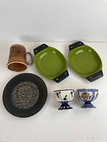 All items in lot displayed with 2 green avocado enamelware dishes, handcrafted ceramic mug with hunting scene, black pottery plate with skull design, and 2 small Poland pottery cups