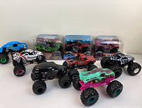 Nine 1/24 scale monster trucks displayed, six loose and three in original packaging.