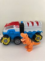 Side view of the Paw Patrol Dino Rescue Truck next to the orange T-rex dinosaur figure showing the full truck and figure size