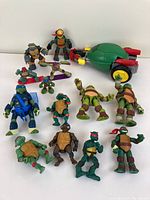 Full lot of Teenage Mutant Ninja Turtles figures displayed on white surface showing 13 figures and 1 toy vehicle.