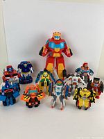 Front view showing eleven Transformers figures in robot form with bright primary colors; some are humanoid robots, others more mechanical.