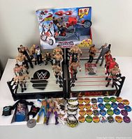 Wide shot showing all 23 WWE wrestling figures arranged on and around two wrestling rings, 6 championship belts laid in front, and 30 power chips in colorful rows. Includes the Wrecking Slamcycle toy in its packaging in the background.