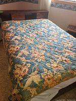 Antique quilted blanket spread on bed showing full floral pattern and wear.