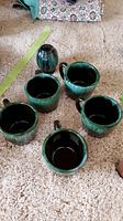 Photo showing five Blue Mountain Pottery mugs and one salt shaker on carpet with blue-green glaze and speckled finish.