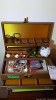 Full view of open wooden jewelry box showing compartments filled with diverse costume jewelry pieces, pins, necklaces, and small ceramic piggy bank.
