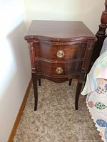 Front view showing two curved drawers with round brass handles, sculpted legs and polished wood finish.