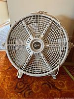 Front view of a large white plastic circular floor fan with metal guard and multiple blades.