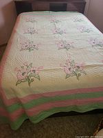 Quilt on bed with pink flower embroidery and striped border in pink and green