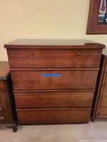 Front view of the four-drawer medium brown wooden mid-century dresser showing drawer fronts and brass knobs.
