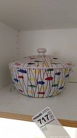 Photo of retro style pot with colorful abstract pattern on a shelf.