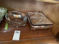 Photo showing Pyrex glass bowl beside a silver plated bowl holder and a double server with glass bowls with lids under a cabinet.
