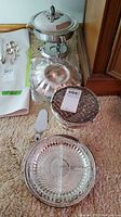Multiple silver serving dishes arranged on carpet, showing chafing dish, divided plate, latticework dish, and pie server.
