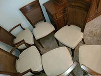 Six wood dining chairs arranged in group, showing cane backs and beige upholstered seats.