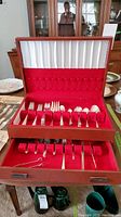 Open wooden two-tier flatware chest showing red velvet lining and assorted pieces