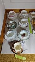 Seven assorted tea cup and saucer sets arranged on a surface, displaying a variety of floral and decorative china patterns.