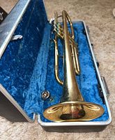 Trumpet laying in open blue velvet-lined hard case showing overall instrument and mouthpiece.