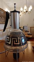 Front view of the vintage mid century coffee carafe showing clear glass body with black Greek Key design, metal neck/lid, black handle, and part of metal stand base with heating element.