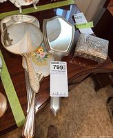 Photo showing three handheld vintage vanity mirrors and one standing mirror on a wooden table.