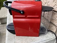 Side view of the red Breville Nespresso Inissia coffee machine showing the glossy red body, black handle and water reservoir tank.