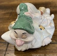 Close-up of Sleepy figurine face with green hat and tongue out lying on a pillow, showing fine detailing and glazing.
