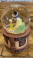 Front view of Disney Store Snow White and Dopey snowglobe inside clear globe on decorative brown base showing Snow White reading a letter to Dopey.